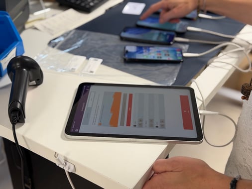 Poste de test et de diagnostic en atelier Phoner : tablette de contrôle, scanner code-barres et smartphones reconditionnés en cours de vérification