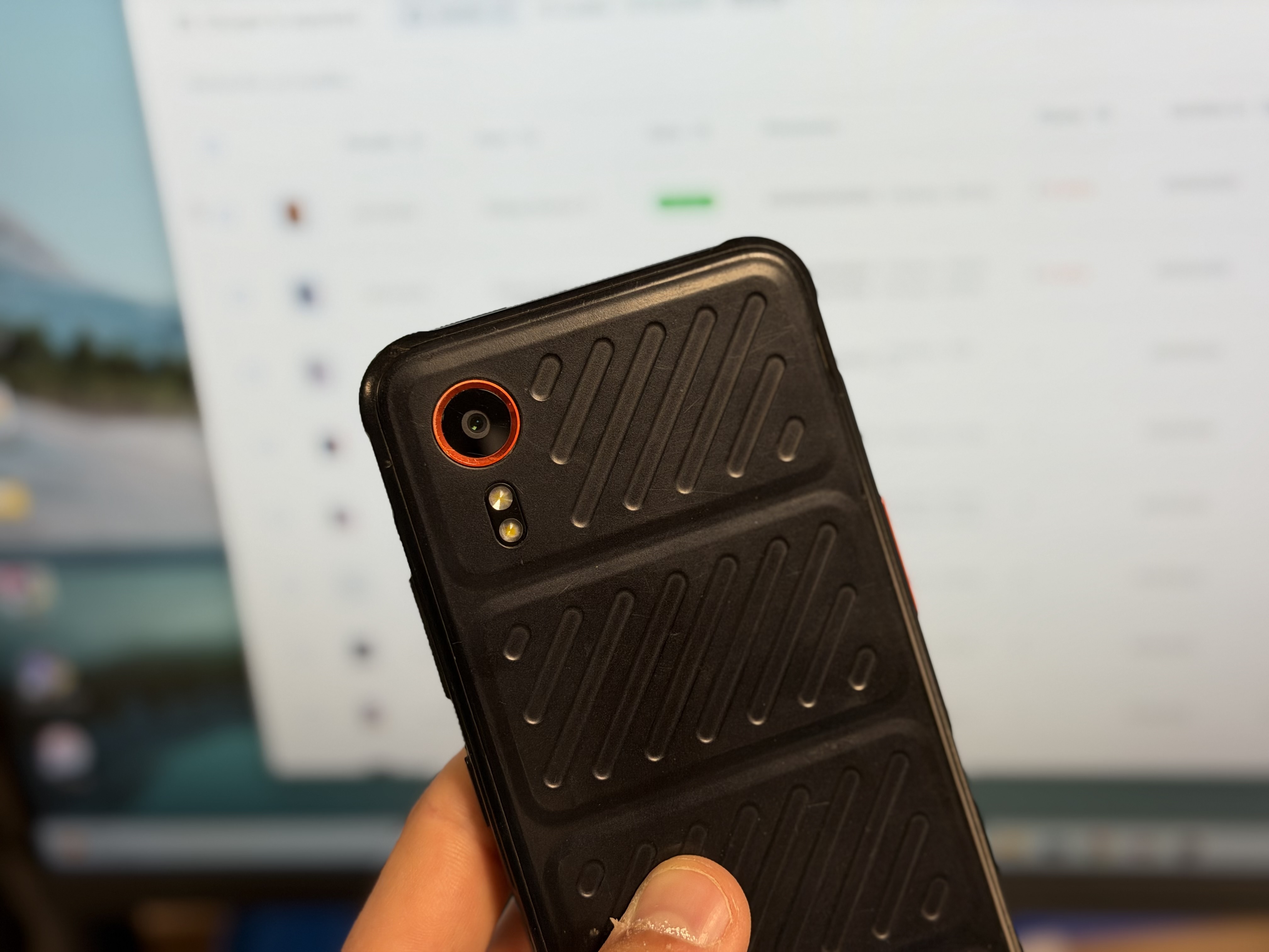 Smartphone durci de flotte mobile professionnelle tenu en main devant un écran de gestion de parc